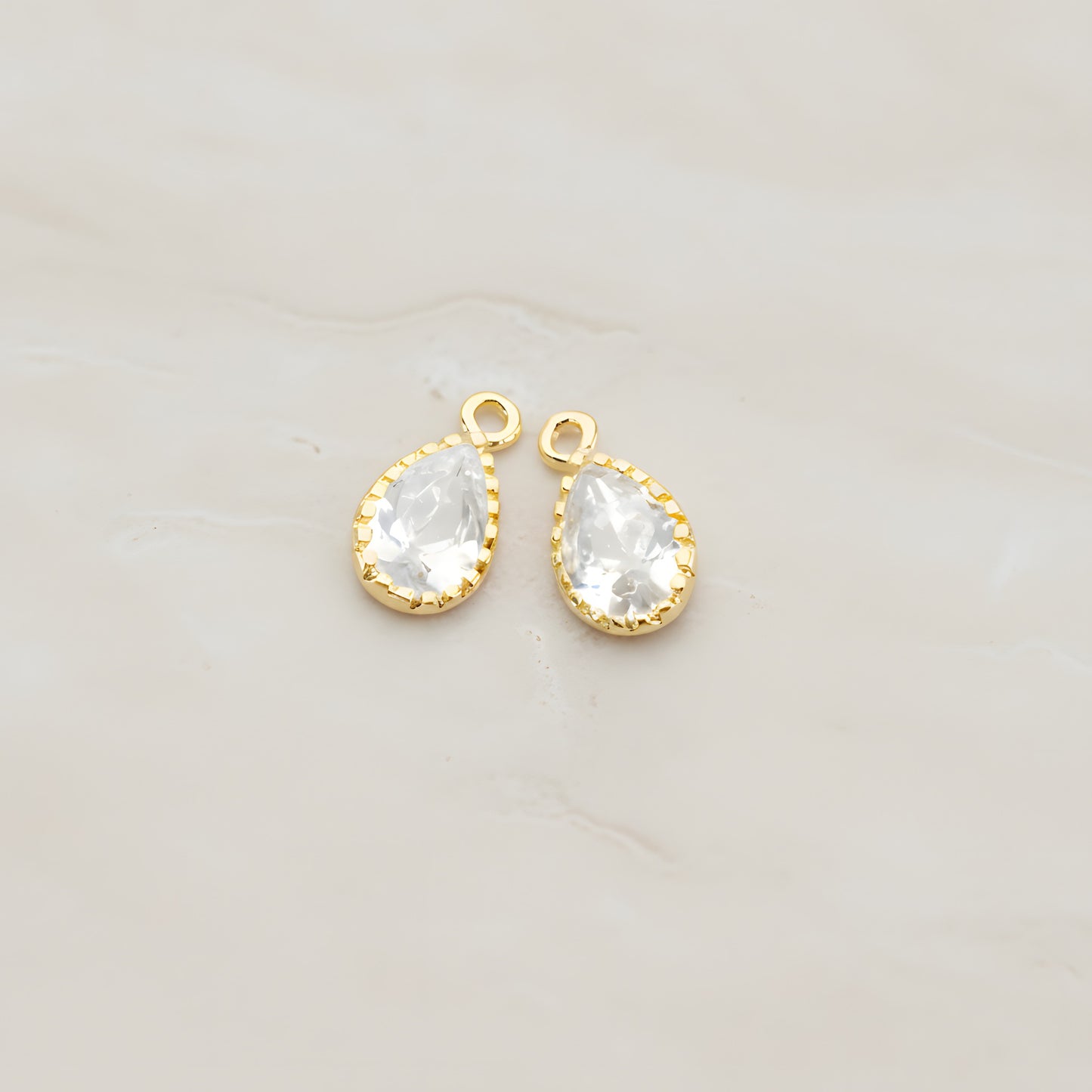 Two teardrop framed glass pendants, each a faceted glass stone set in a beaded brass bezel with a single top loop