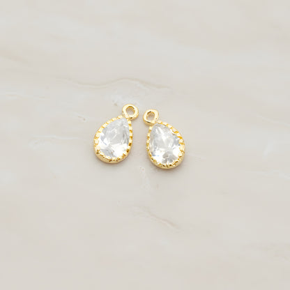 Two teardrop framed glass pendants, each a faceted glass stone set in a beaded brass bezel with a single top loop