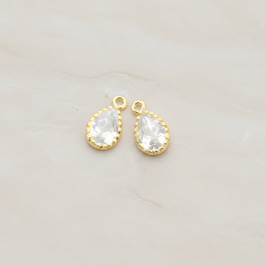 Two teardrop framed glass pendants, each a faceted glass stone set in a beaded brass bezel with a single top loop