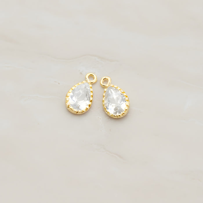 Two teardrop framed glass pendants, each a faceted glass stone set in a beaded brass bezel with a single top loop