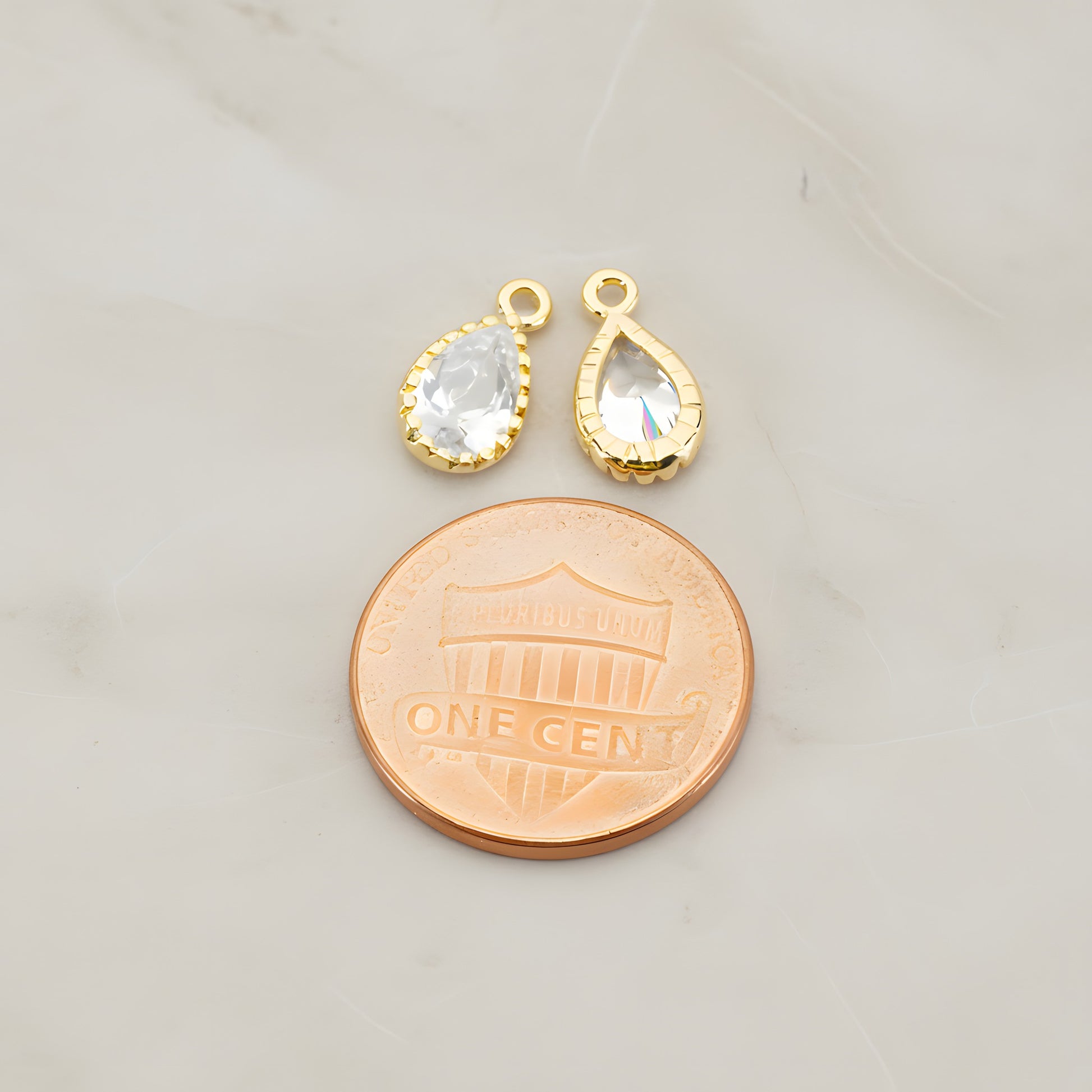 Two teardrop framed glass pendants, each a faceted glass stone set in a beaded brass bezel with a single top loop