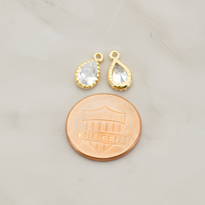 Two teardrop framed glass pendants, each a faceted glass stone set in a beaded brass bezel with a single top loop